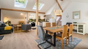 A spacious living area with a high ceiling, skylights, a dining table with chairs, a sofa, and a kitchen in the background. - Haus Wiesenruhe Apartment 1 – Modern & Cozy (Seebach)