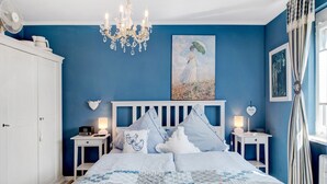 Ein Schlafzimmer mit Bett, Nachttischen, einer Chandelieber, Kunstwerken und einem Fenster mit Vorhängen.