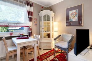 A room with a dining table, chairs, a cabinet, a television, and a window with curtains.