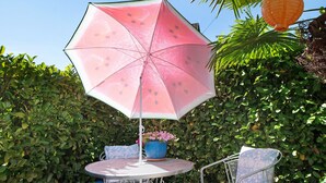 Ein runder Metalltisch mit einem Topfpflanzen, einem pinken Sonnenschirm und einem Metallstuhl mit Kissen.