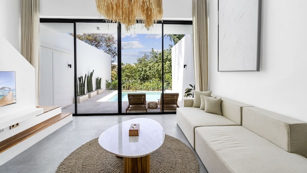 Ein modernes Wohnzimmer mit großem Fenster, einem weißen Sofa, einem Couchtisch und Blick auf einen Außenpool.
