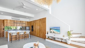 Eine moderne Küche mit Holzelementen, ein Essbereich mit rundem Tisch und ein Wohnbereich mit Fernseher und Treppe.