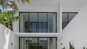 Ein modernes, zweistöckiges Haus mit Swimmingpool, zwei Liegestühlen und einer Reihe von Kakteen.