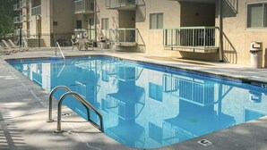 A swimming pool with a metal ladder, surrounded by a concrete deck and a building with balconies. - 5 mins to Dollywood - Hideaway Waters 5ppl Condo (Pigeon Forge)