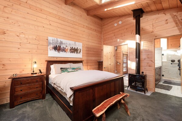 Un dormitorio de cabaña de madera con cama, mesita de noche, lámpara y un cuadro de caballos.