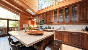 A modern kitchen with wooden cabinets, a large island, and a view of the outdoors. - Modern Mountain Retreat w/ Amazing Views • Hot Tub • Deck • Pets Welcome (Idyllwild-Pine Cove)