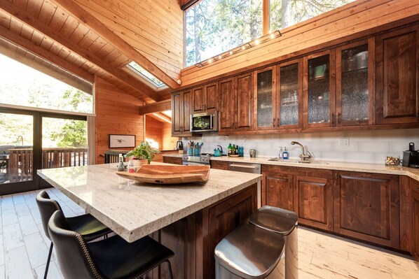 A modern kitchen with wooden cabinets, a large island, and a view of the outdoors.