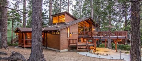 Een chalet met terras, omringd door hoge bomen.