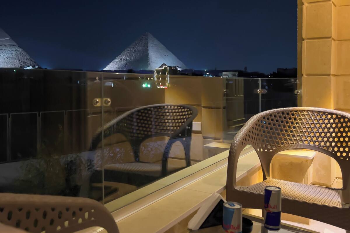 A balcony with two wicker chairs, a glass partition, and a view of pyramids at night.