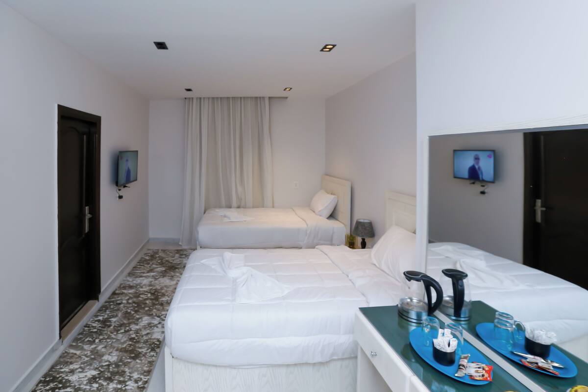 A hotel room with two beds, a small table with a tray of breakfast items, and a TV mounted on the wall.