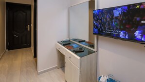 A hotel room with a flat-screen TV mounted on the wall, a desk with a telephone, remote controls, and a mirror. - Pyramids land hotel (Giza)