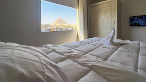 A hotel room with a bed, a window with a view of the pyramid, and a TV on the wall. - Pyramids land hotel (Giza)