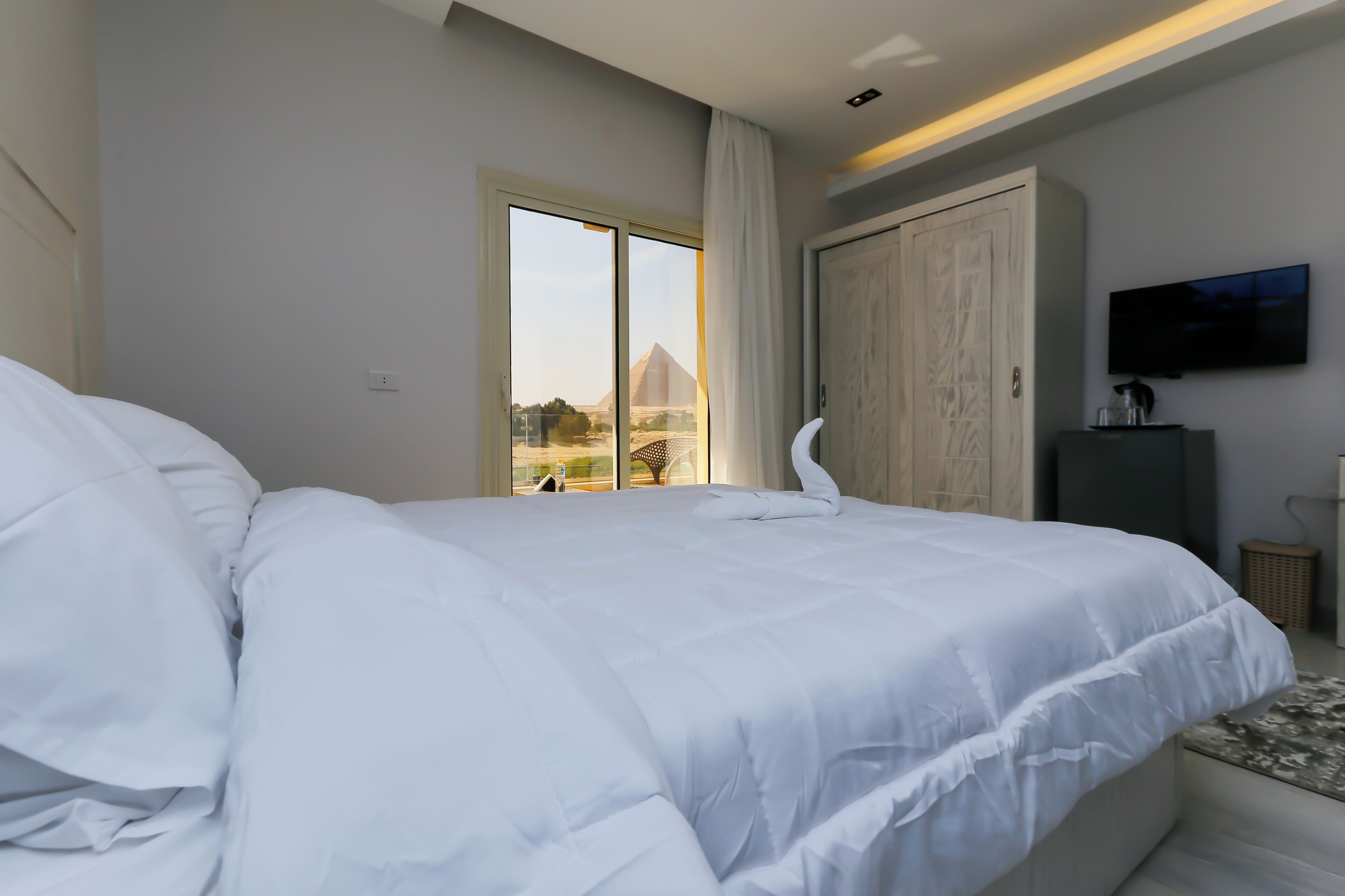 A hotel room with a large bed, a sliding glass door leading to a balcony, a television mounted on the wall, and a wardrobe.