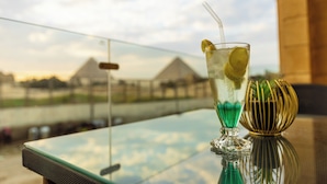 A glass with a straw and lime slice on a reflective surface with a clear view of pyramids in the background. - Pyramids land hotel (Giza)