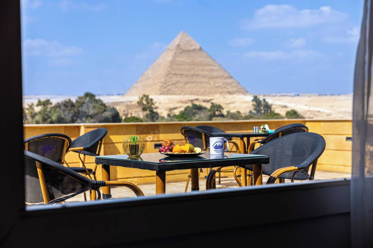A table with chairs and a view of the Great Pyramid of Giza.