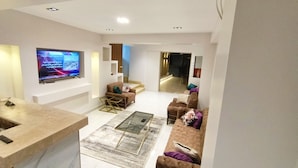 A modern living room with a flat-screen TV, sofas, a coffee table, and a kitchen area. - Pyramids land hotel (Giza)