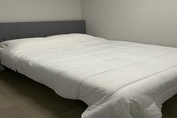 A single bed with a grey headboard in a room with plain walls and a tiled floor.