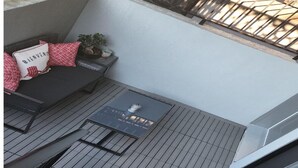 Un balcón con una mesa negra, un sofá con cojines rojos y una planta en maceta.