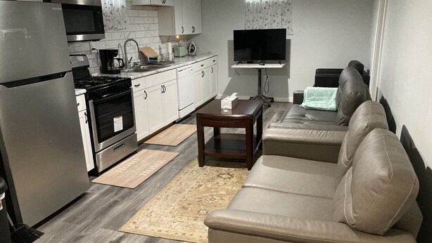 Et moderne køkken med stålemmer, et spiseområde med sofa og sofabord, og et fladskærms-tv ophængt på væggen.