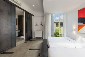 Ein modernes Hotelzimmer mit einem großen Bett, einem begehbaren Kleiderschrank, einem Badezimmer mit Waschbecken und Spiegel sowie Blick ins Freie.