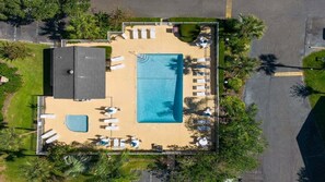 Vue aérienne d’un complexe hôtelier doté d’une grande piscine, de chaises longues et de palmiers.