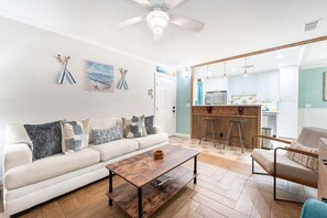 Un salon avec un canapé, une table basse et, au fond, un coin cuisine.