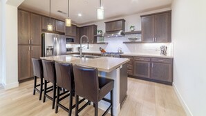 A modern kitchen with dark wooden cabinets, a central island with bar stools, stainless steel appliances, and pendant lighting.