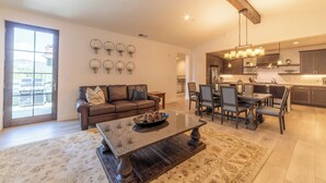 A spacious living room with a brown leather sofa, a dark wooden coffee table, and a dining area with a chandelier.