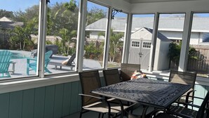 A covered patio with a table and chairs, large windows, and a view of a swimming pool and houses. - 3 Bed 2 Bath House - Blocks to the Beach - 40 Foot Pool! (Cape Canaveral)
