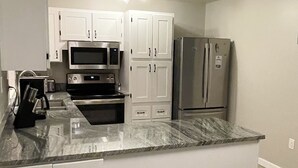 A kitchen with white cabinets, stainless steel appliances, and a marble countertop. - 3 Bed 2 Bath House - Blocks to the Beach - 40 Foot Pool! (Cape Canaveral)