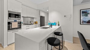 A modern kitchen with white cabinetry, a central island, a microwave, and a sink.