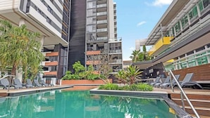 A swimming pool with lounge chairs, surrounded by modern buildings with balconies.