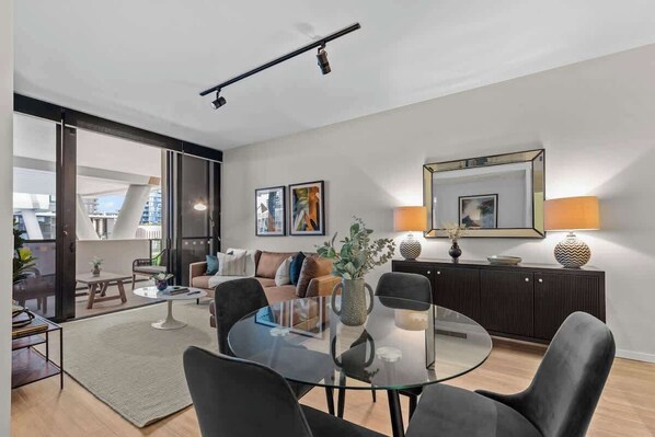 A modern living room with a glass coffee table, a sofa, and a dining area with a glass table.
