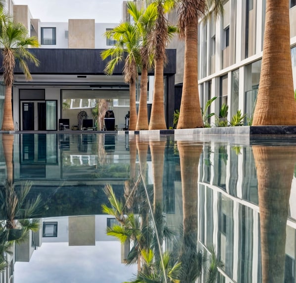 Un edificio moderno con un estanque reflectante, palmeras y fachada de vidrio.