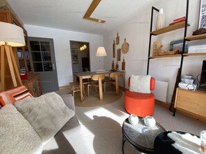 Uma sala de estar moderna com um sofá, uma mesa de jantar com cadeiras, um banquinho vermelho e uma estante de livros.