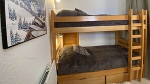 Una cama litera con escalera, un cuadro en la pared y una ventana con cortinas.