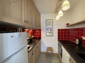 Una cucina con mobili in legno, un frigorifero bianco, zoccolo di piastrelle rosse e lampade a sospensione.