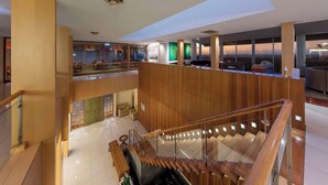 Un moderno vestíbulo de hotel con una escalera de cristal, paneles de madera y vistas a la ciudad.