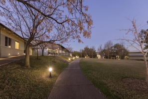 A pathway leading to a building with a modern architectural style, a grassy area, and trees with autumn foliage. - Elysia Wellness Retreat (Pokolbin)