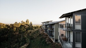 Un edificio moderno de varios pisos con balcones, ventanas amplias y vistas a una colina boscosa.