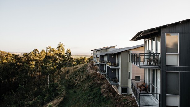 A modern multi-story building with balconies, large windows, and a view of a forested hill. - Elysia Wellness Retreat (Pokolbin)