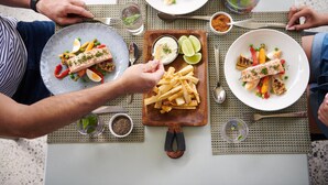 A dining table with multiple plates of food, including salmon, vegetables, and fries. - Elysia Wellness Retreat (Pokolbin)