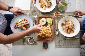 A dining table with multiple plates of food, including salmon, vegetables, and fries. - Elysia Wellness Retreat (Pokolbin)