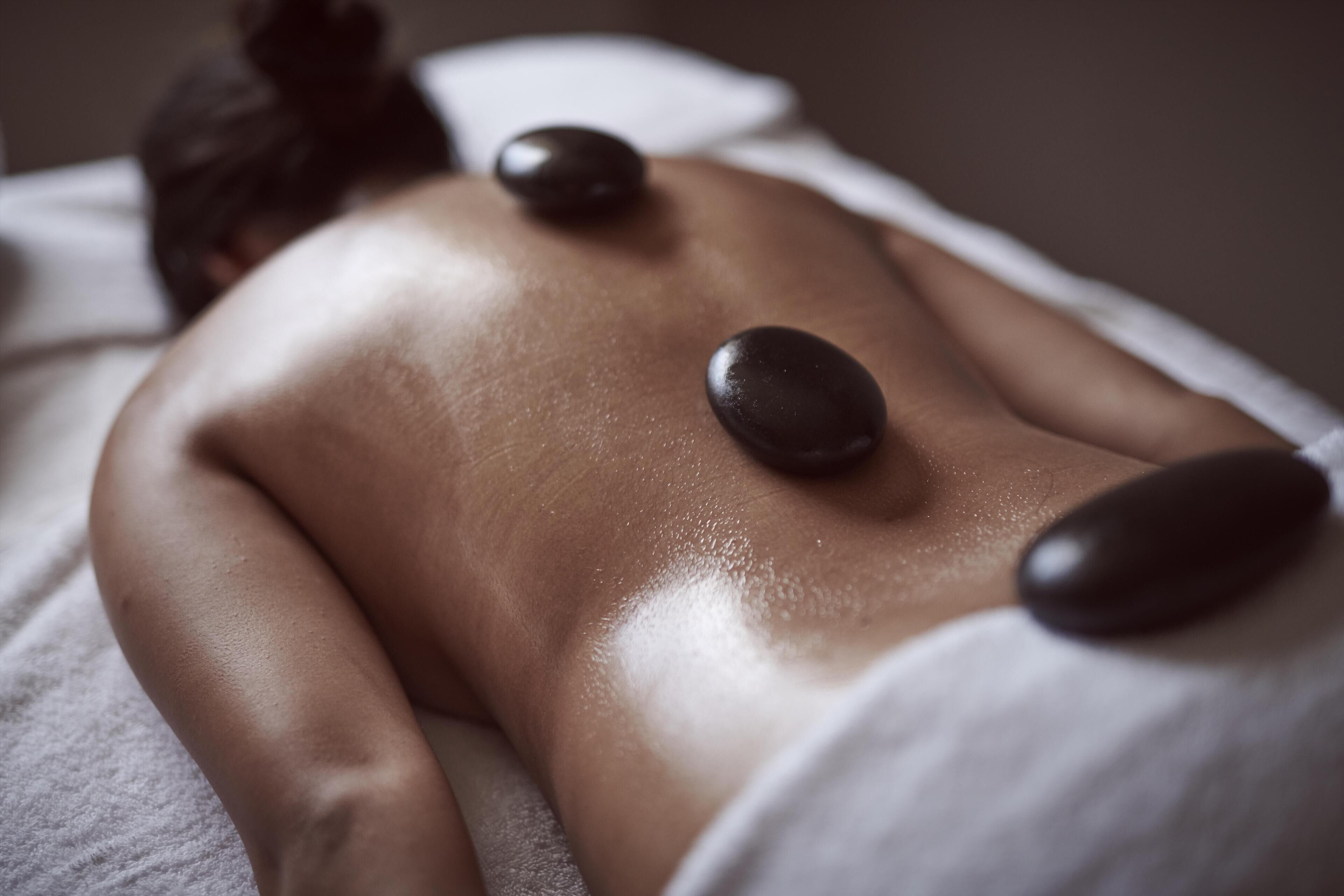 Une personne reçoit un massage du dos avec trois pierres chaudes placées sur le dos.