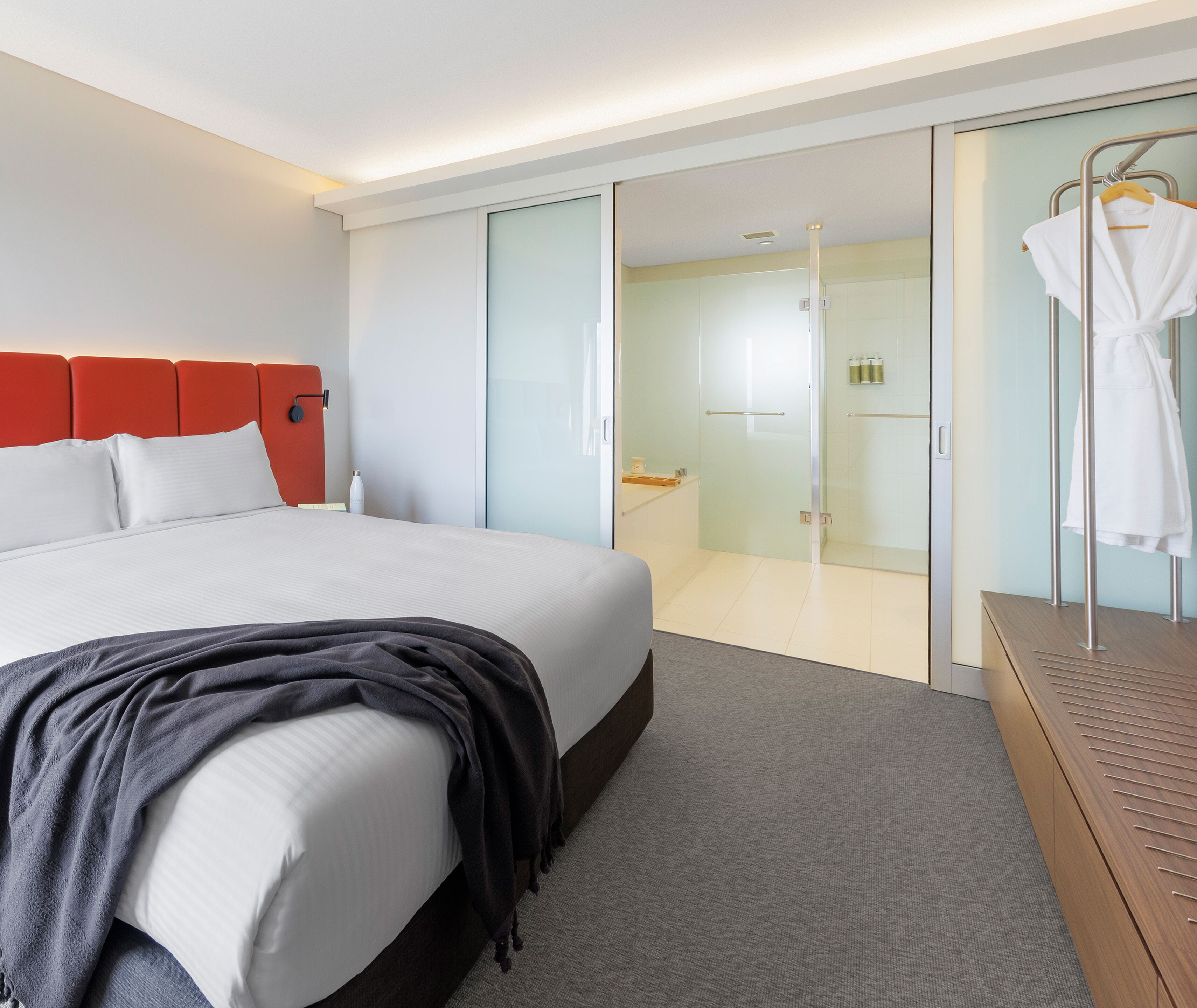 A modern hotel room with a large bed, a walk-in closet, and a glass shower area.