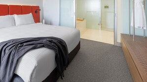A modern hotel room with a large bed, a walk-in closet, and a glass shower area.