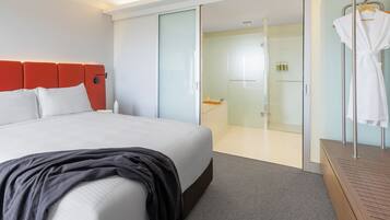 A modern hotel room with a large bed, a walk-in closet, and a glass shower area.