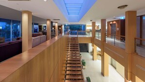 Un moderno vestíbulo de hotel con una escalera central, ventanas amplias y un tragaluz.