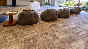 A conference room with a carpeted floor, bean bags, a projector screen, a podium, and a table with a plant.
