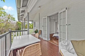 Un porche cubierto con una mesa y sillas, un sofá, y puertas abiertas que dan a una habitación.